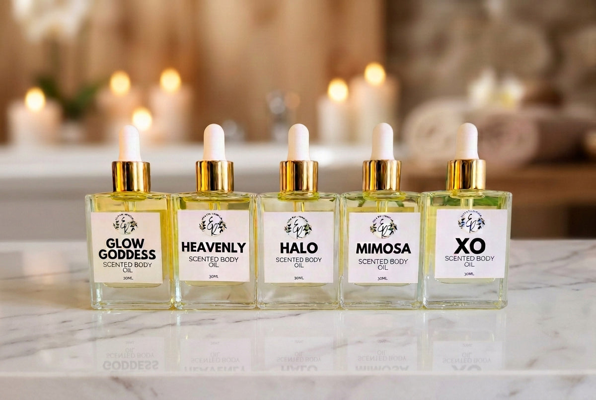 Five glass bottles with gold caps and labels on a white surface with greenery.
