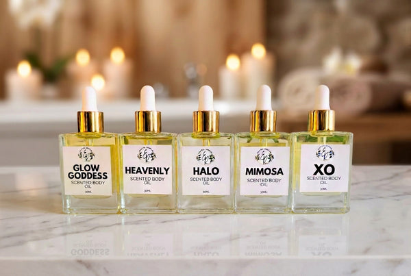 Five glass bottles with gold caps and labels on a white surface with greenery.